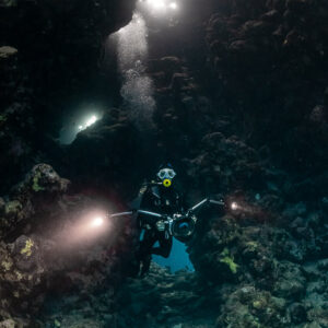 Divers with torches in a cave beneath bright openings, vertical, Shaab Claudio, Red Sea, Egypt