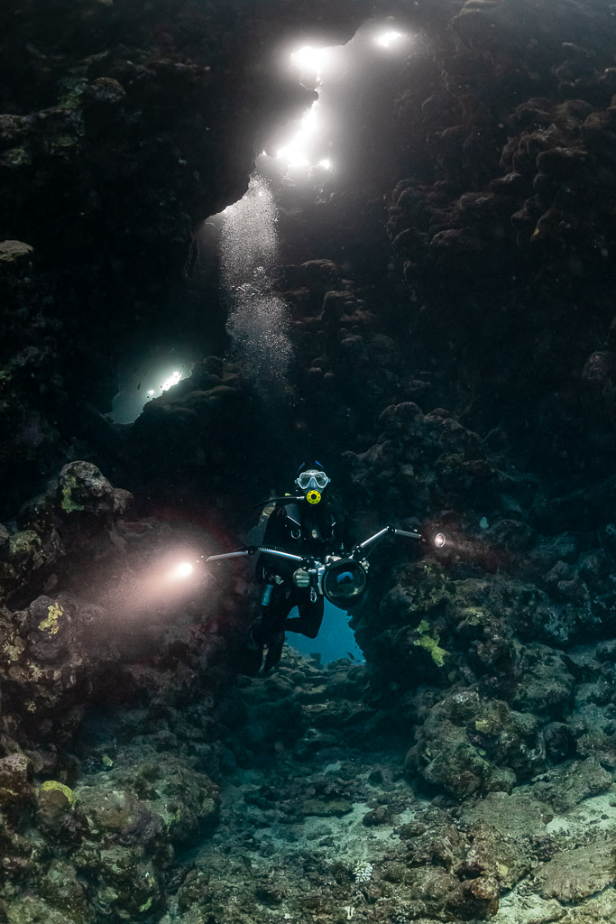 Divers with torches in a cave beneath bright openings, vertical, Shaab Claudio, Red Sea, Egypt