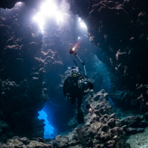 Diver silhouetted in a cave with blue exit and bright roof holes, Shaab Claudio, Red Sea, Egypt