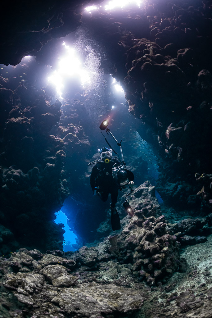 Diver silhouetted in a cave with blue exit and bright roof holes, Shaab Claudio, Red Sea, Egypt