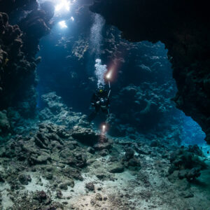 Divers with torches in a wide cave chamber, horizontal view, Shaab Claudio, Red Sea, Egypt
