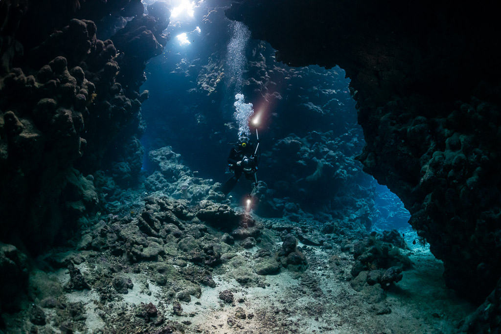 Divers with torches in a wide cave chamber, horizontal view, Shaab Claudio, Red Sea, Egypt
