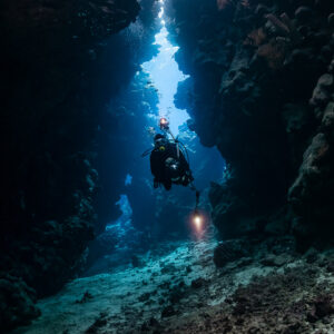 Diver in a narrow vertical cave fissure lit by blue light, Shaab Claudio, Red Sea, Egypt