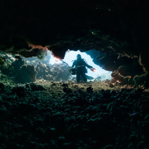 Diver silhouetted in a low cave entrance seen from inside, Shaab Claudio, Red Sea, Egypt