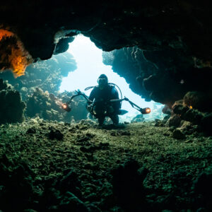 Underwater photographer with strobes kneeling at a cave opening, Shaab Claudio, Red Sea, Egypt