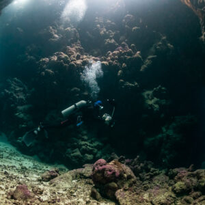 Diver exploring a sandy cave chamber with light from above, Shaab Claudio, Red Sea, Egypt