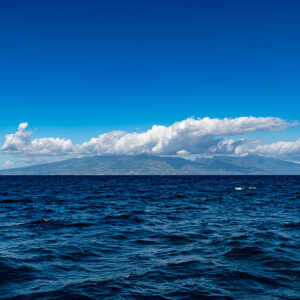 Distant island under white clouds seen across the open ocean, Tahiti, Society Islands, French Polynesia