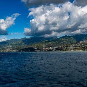 Green mountains and coastal town seen from the sea under dramatic clouds, Tahiti, Society Islands, French Polynesia