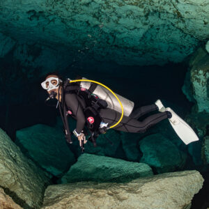 Cavern diver with yellow long hose swimming between limestone boulders, Quintana Roo, Mexico