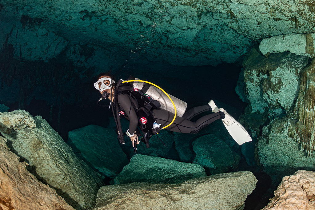 Cavern diver with yellow long hose swimming between limestone boulders, Quintana Roo, Mexico