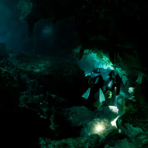Group of divers with torches entering a cenote cavern from the light zone, Quintana Roo, Mexico