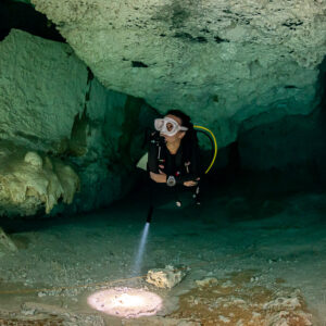 Cavern diver facing the camera, torch beam spotlighting the sandy floor, Quintana Roo, Mexico