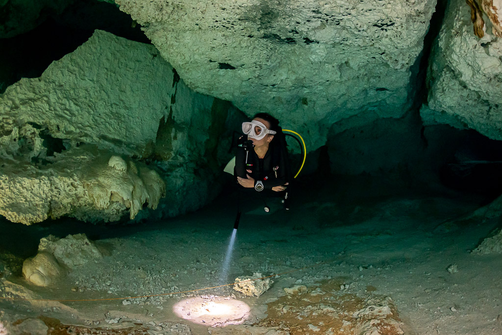 Cavern diver facing the camera, torch beam spotlighting the sandy floor, Quintana Roo, Mexico