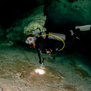 Cavern diver swimming under a low limestone ceiling, torch pointing down, Quintana Roo, Mexico