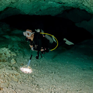 Cavern diver emerging from a dark low passage with torch on the floor, Quintana Roo, Mexico