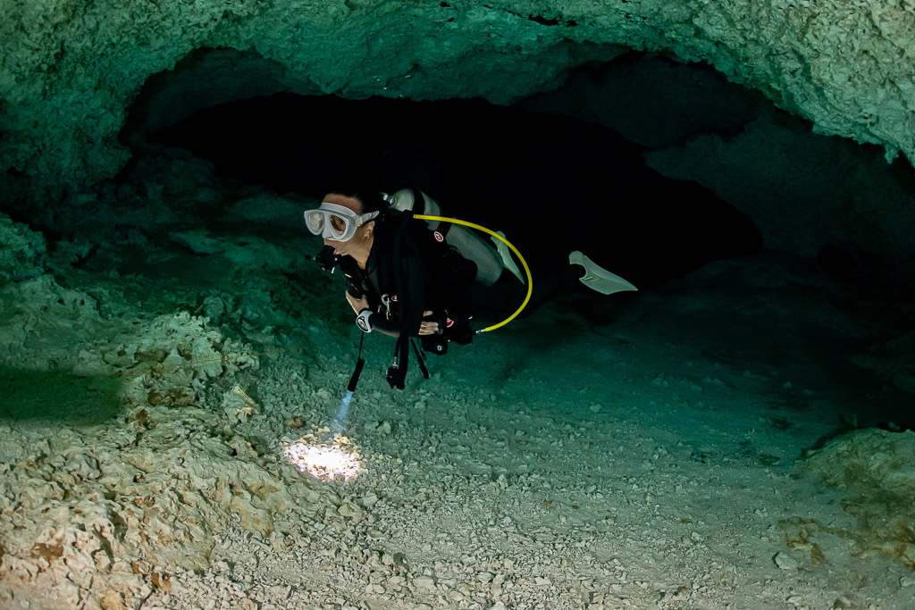 Cavern diver emerging from a dark low passage with torch on the floor, Quintana Roo, Mexico