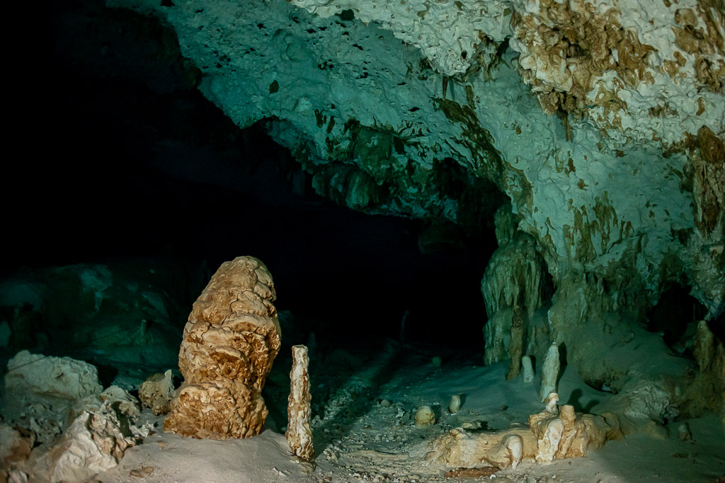 Orange stalagmite and pale speleothems in an empty cenote chamber, Quintana Roo, Mexico