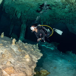 Cavern diver gliding past thin columns over an orange rock formation, Quintana Roo, Mexico