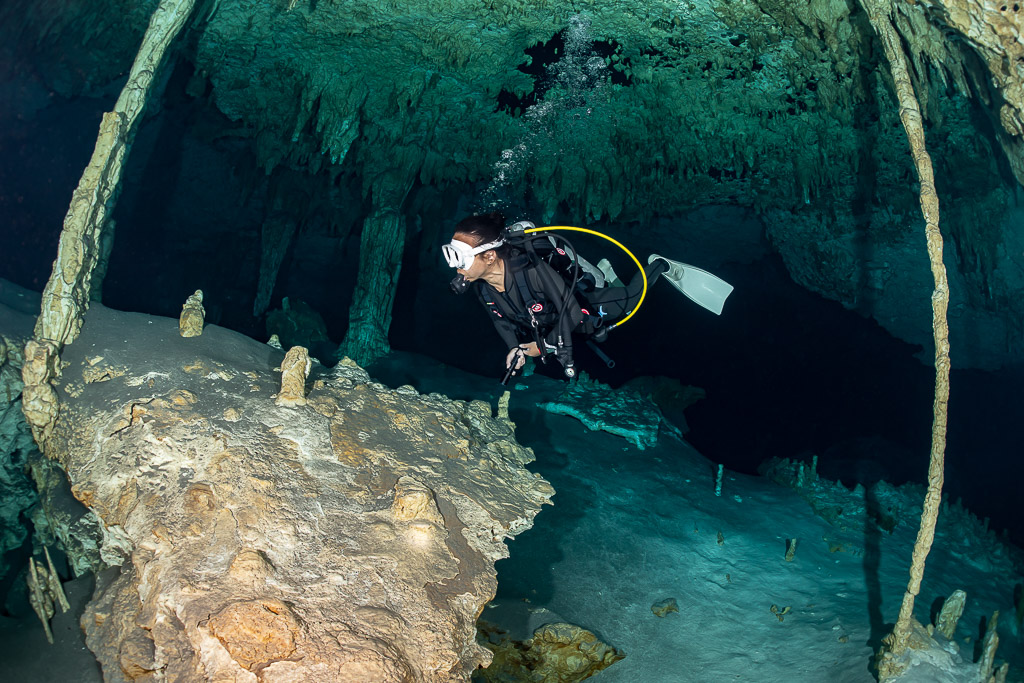 Cavern diver gliding past thin columns over an orange rock formation, Quintana Roo, Mexico