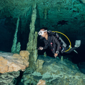 Cavern diver swimming between stalagmite columns, close side view, Quintana Roo, Mexico