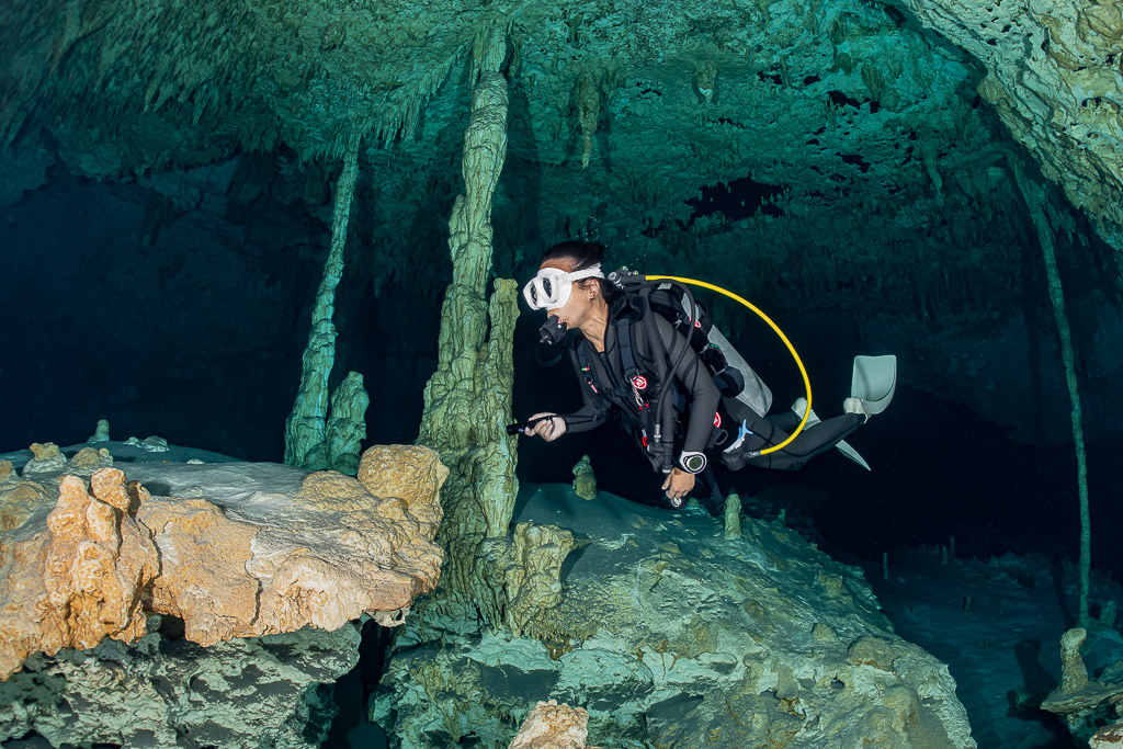 Cavern diver swimming between stalagmite columns, close side view, Quintana Roo, Mexico