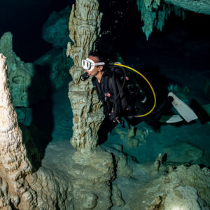 Cavern diver behind a tall white stalagmite in a decorated cenote room, Quintana Roo, Mexico