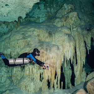 Sidemount cave diver passing a wall of curtain-like stalactites along the guideline, Quintana Roo, Mexico