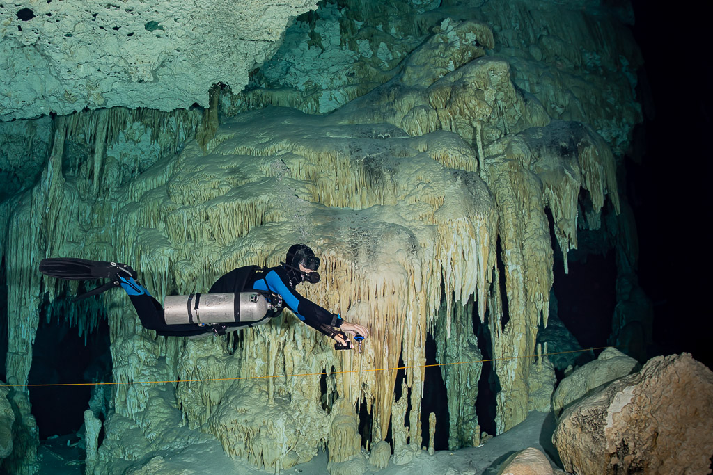Sidemount cave diver passing a wall of curtain-like stalactites along the guideline, Quintana Roo, Mexico