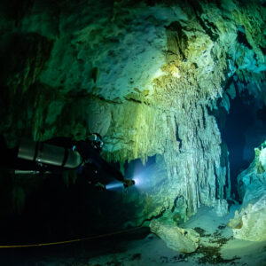 Diver with torch lighting a green-yellow limestone wall in a cenote cavern, Quintana Roo, Mexico