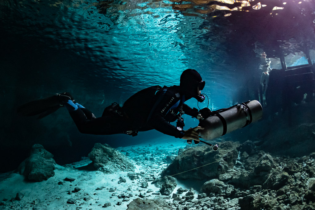 Sidemount diver in silhouette under the mirrored surface of a cenote, Quintana Roo, Mexico