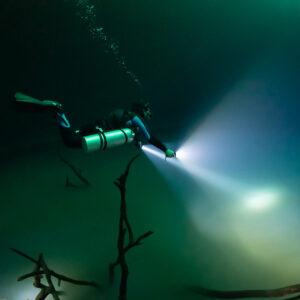 Sidemount diver lighting the hazy layer below sunken branches, Cenote Angelita, Quintana Roo, Mexico