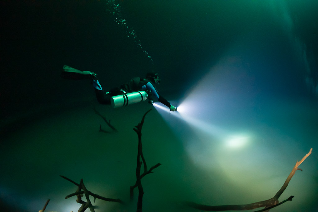 Sidemount diver lighting the hazy layer below sunken branches, Cenote Angelita, Quintana Roo, Mexico