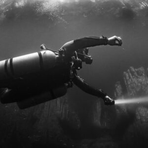 Black and white close view of a sidemount diver reaching forward with torch, Quintana Roo, Mexico