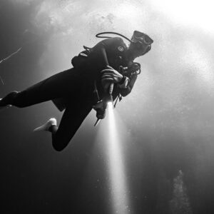 Black and white low-angle view of a diver with torch against bright water, Quintana Roo, Mexico