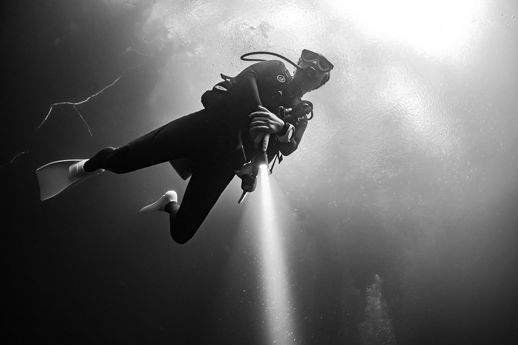 Contre-plongée en noir et blanc d’un plongeur avec phare sur fond d’eau claire, Quintana Roo, Mexique