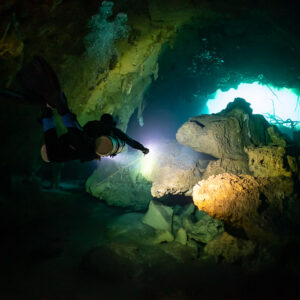 Diver lighting a large boulder at the mouth of a cenote cavern, Quintana Roo, Mexico
