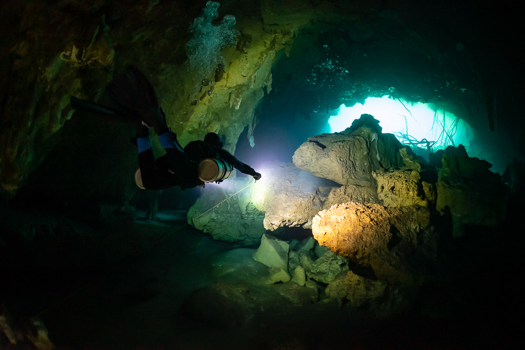 Diver lighting a large boulder at the mouth of a cenote cavern, Quintana Roo, Mexico