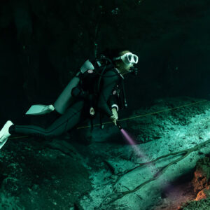 Cavern diver with torch following the line along a green sloping wall, Quintana Roo, Mexico