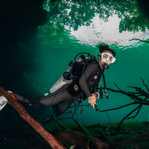 Cavern diver posing among sunken branches in a shallow sunlit cenote, Quintana Roo, Mexico