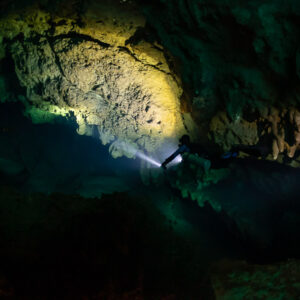 Diver with torch lighting a yellow ceiling in a dark cavern, Quintana Roo, Mexico