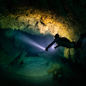 Diver in silhouette lighting a passage beneath a golden lit ceiling, Quintana Roo, Mexico