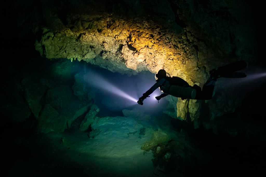 Diver in silhouette lighting a passage beneath a golden lit ceiling, Quintana Roo, Mexico
