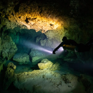 Diver with torch crossing a rocky cavern beneath a yellow ledge, Quintana Roo, Mexico