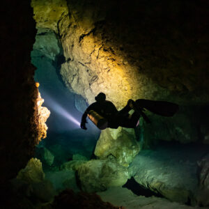 Vue verticale d’un plongeur avec phare dans une galerie aux tons dorés, Quintana Roo, Mexique