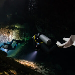 Two divers in a dark cave, close fins in the foreground, torch lit floor, Quintana Roo, Mexico