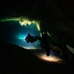 Two cave divers entering a passage under stalactites, one in silhouette, Quintana Roo, Mexico