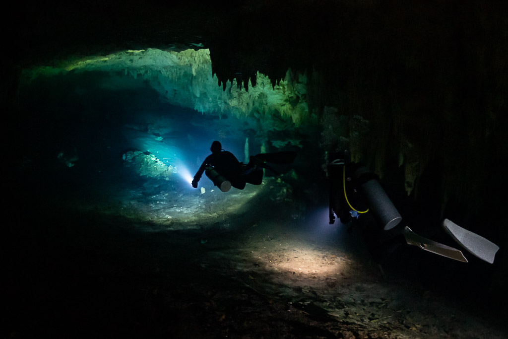 Two cave divers with torches heading into a blue-lit cave passage, Quintana Roo, Mexico