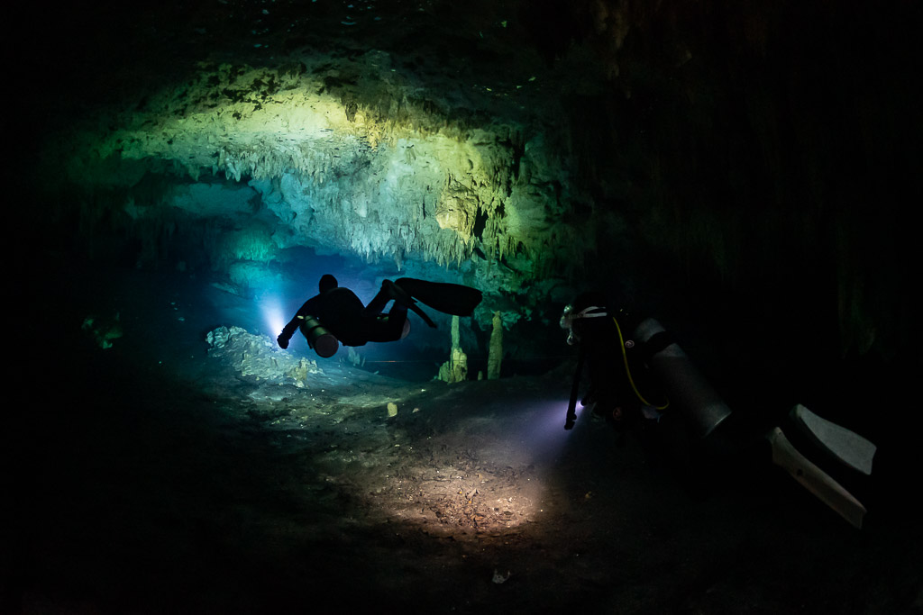 Two divers with torches in a dark decorated cave, wide view, Quintana Roo, Mexico