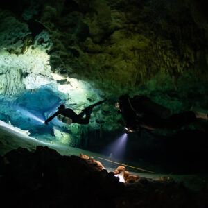 Two divers in silhouette lighting a cave tunnel with green walls, Quintana Roo, Mexico