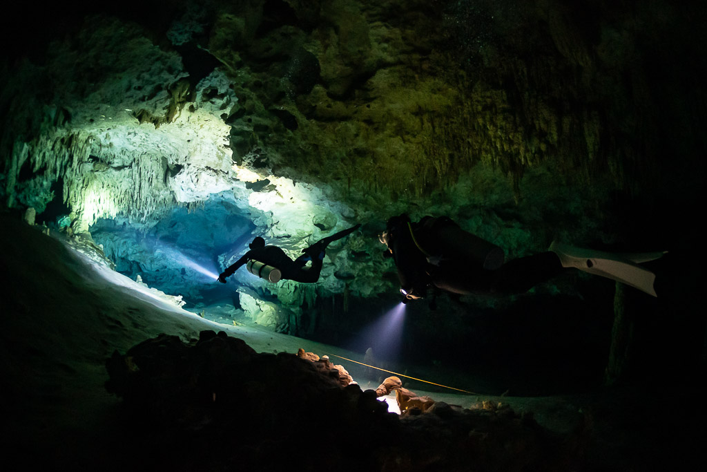 Two divers in silhouette lighting a cave tunnel with green walls, Quintana Roo, Mexico